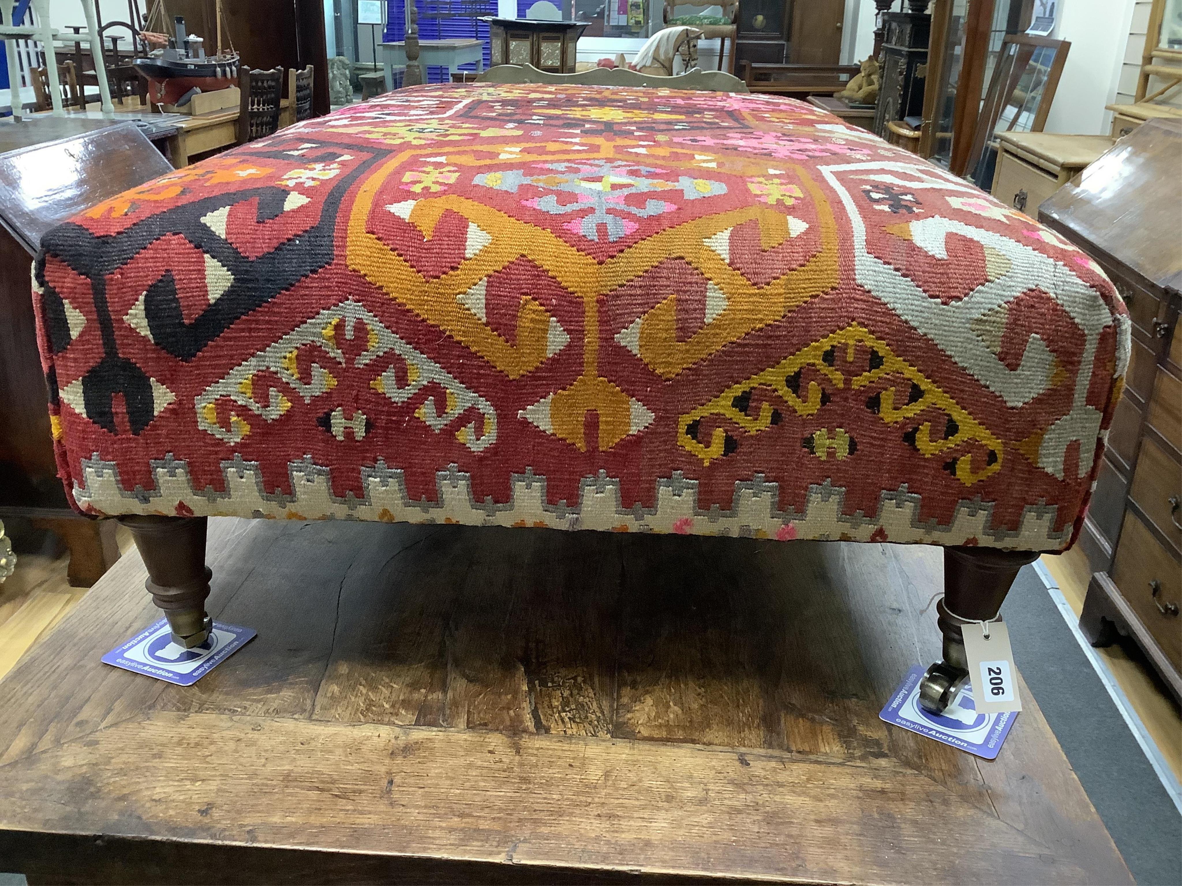 A large contemporary rectangular footstool with antique polychrome Kilim upholstery on turned beech feet with brass caps and castors, width 124cm, depth 78cm, height 40cm.